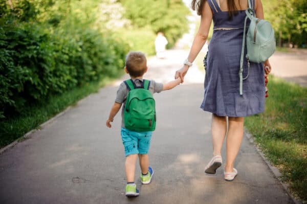 Moeder en zoontje lopen hand in hand. Foto van achteren genomen.